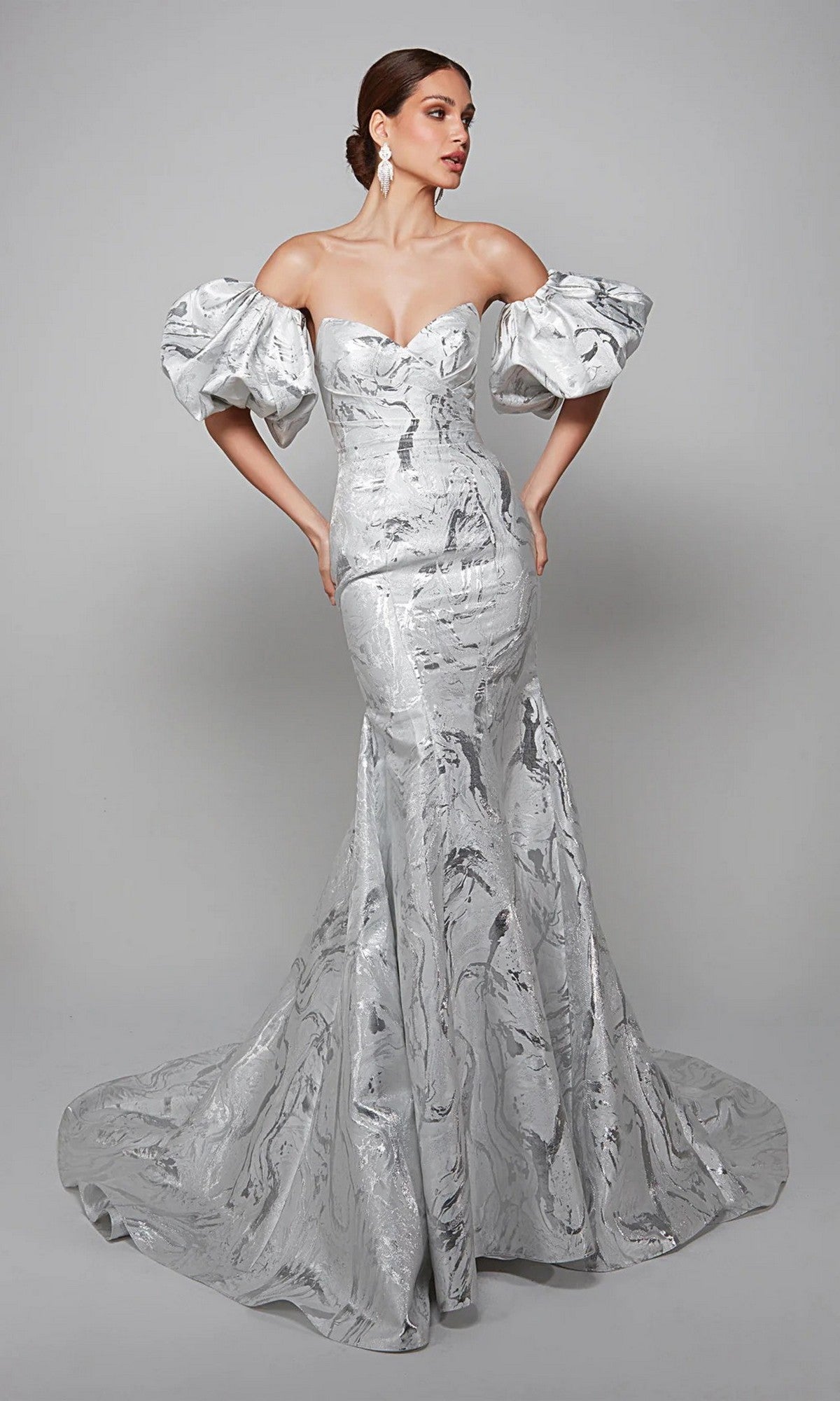 A woman poses in the Alyce 7055 long white dress in ivory/silver, featuring dramatic puffed sleeves and a fitted, flared skirt—a sophisticated mother-of-the-bride look—against a plain gray background.